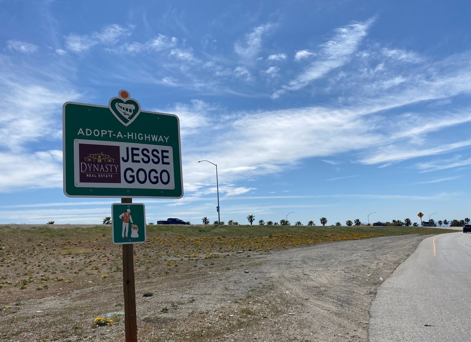 Jesse Gogo Adopt-A-Highway sign on the I-15 Foothill Boulevard on-ramp under a wide blue sky.