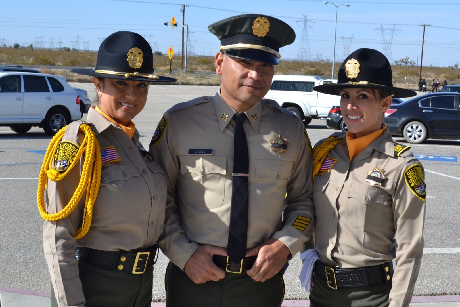 Jesse Gogo in his California Department of Corrections captain uniform, standing between two uniformed officers at an outdoor ceremony.