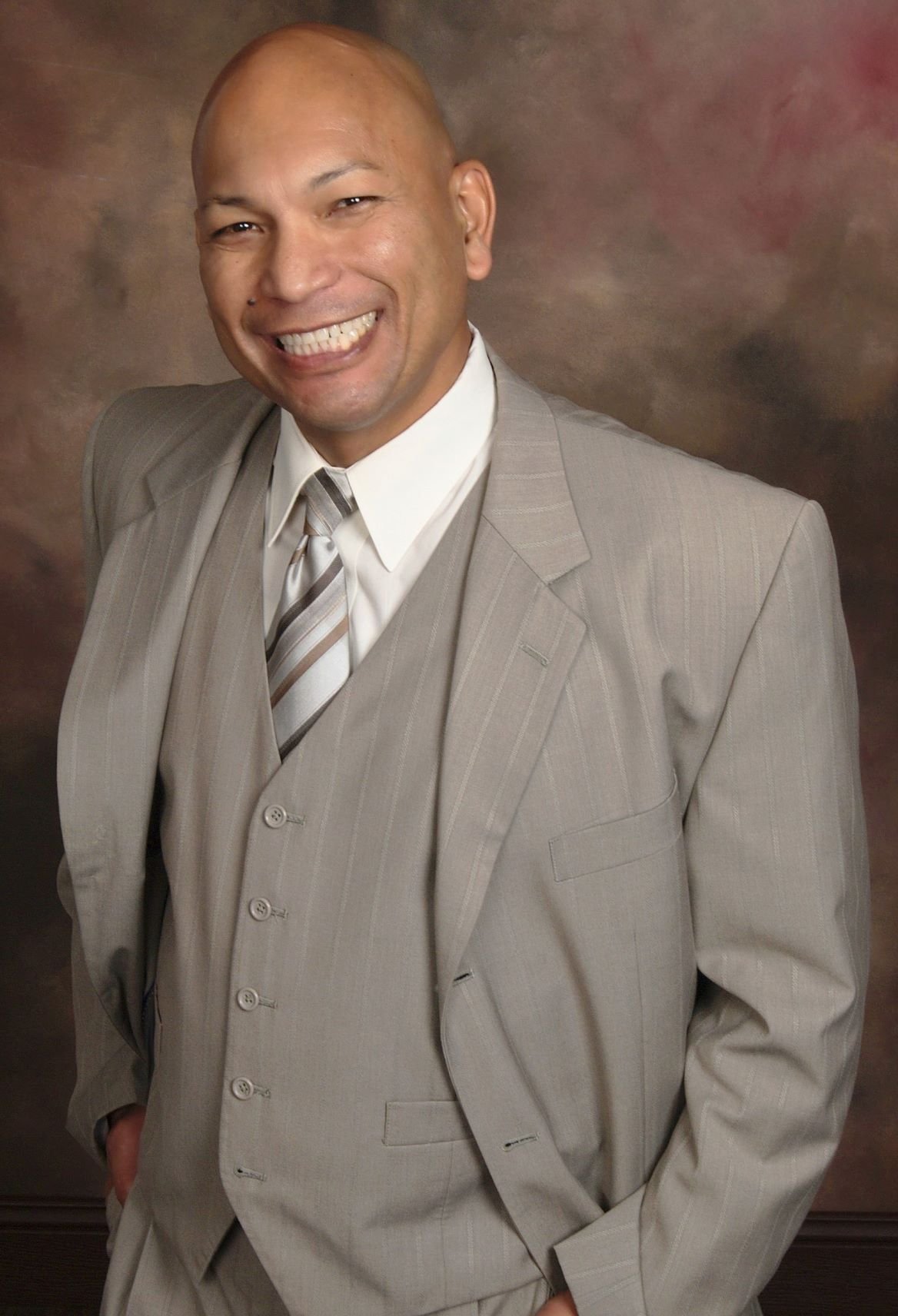 Professional portrait of Jesse Gogo in a light gray three-piece suit, smiling.