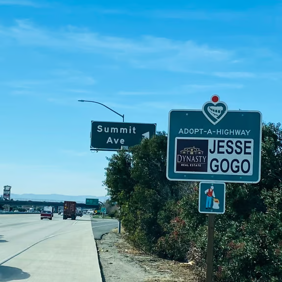 Jesse Gogo Adopt-A-Highway sign beside the Summit Avenue freeway guide sign on a bright blue-sky day.