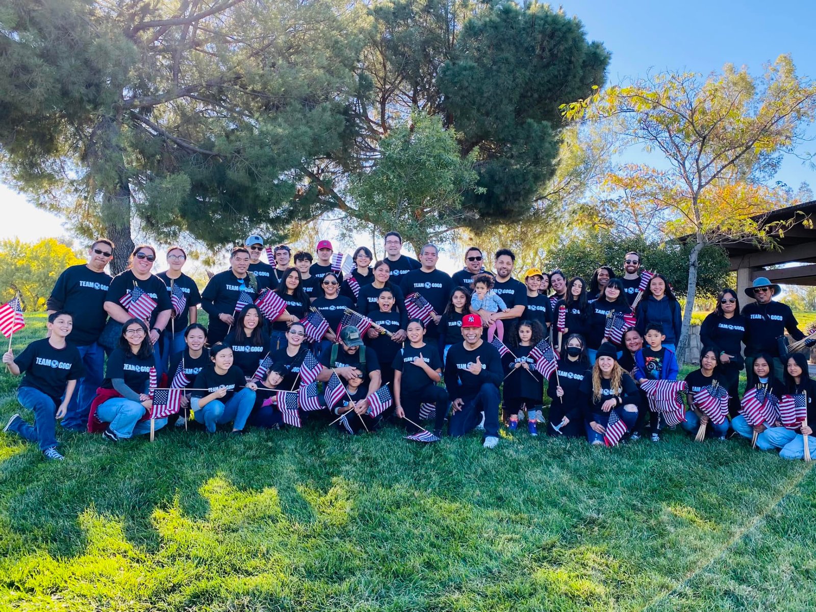 Large TEAM GOGO community group gathered outdoors holding American flags.