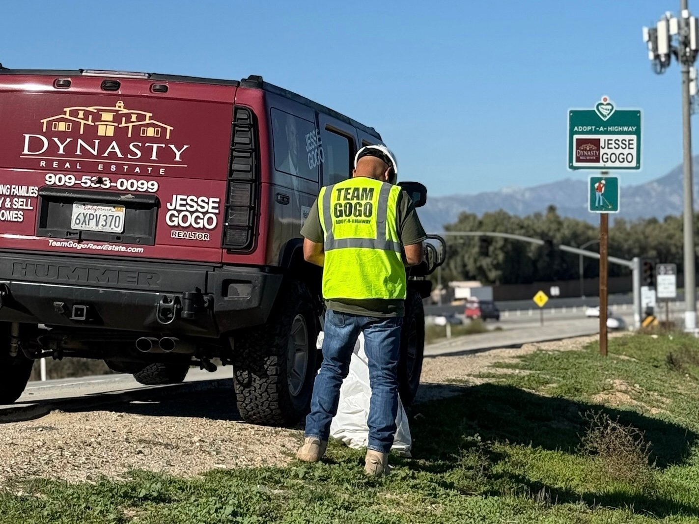 Jesse Gogo collecting roadside litter beside his burgundy Hummer and Adopt-A-Highway sign.